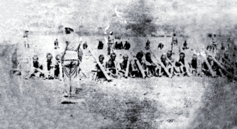 ภาพขาวดำกลุ่มผู้นำและชาวบ้านที่ถูกจับกุม ในฐานะกบฏผู้มีบุญ ณ ทุ่งศรีเมือง จังหวัดอุบลราชธานี เมื่อปี พ.ศ. 2444 ผู้ถูกจับกุมหลายคนถูกใส่ขื่อคา และนั่งอยู่บนพื้นดิน มีทหารสยามยืนควบคุมอยู่ด้านหลัง