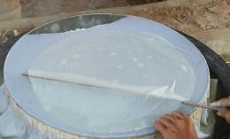 การใช้ไม้แซะแผ่นแป้งที่นึ่งสุกบนผ้าขาวที่ขึงบนปากหม้อ