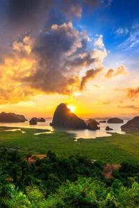 วิวภูเขาและทะเลช่วงพระอาทิตย์ขึ้น ภาพนี้ถ่ายจากมุมสูง มองเห็นทะเลสีฟ้าและเกาะหินปูนรูปร่างสวยงามกระจายอยู่กลางทะเล ด้านล่างสุดของภาพเป็นผืนป่าชายเลนสีเขียวแน่น บนฟ้ามีเมฆสีทองและแสงอาทิตย์ส่องลอดเมฆออกมาอย่างงดงาม บ่งบอกถึงธรรมชาติที่อุดมสมบูรณ์และบรรยากาศสดชื่น