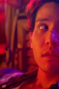 ภาพระยะใกล้ ใบหน้าของพระเอก "แทน" ที่ดูเศร้าและกังวล ภาพมีการเบลอเพื่อให้เห็นมุมมองเลือนรางเหมือนสายตาของเขา ด้านข้างมีข้อความชื่อเรื่อง "Focus เบลอว่ารักแถบ"